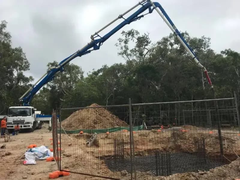 Concrete being poured at a construction site by a blue boom truck, with dirt and rebar visible — Far Northern Concrete Pumping, servicing Tully QLD